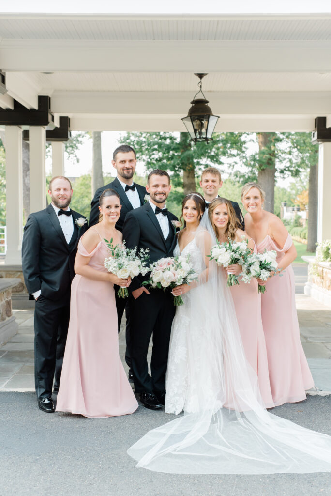 A cute and casual bridal party portrait of a summer wedding with pink gowns and black suits.