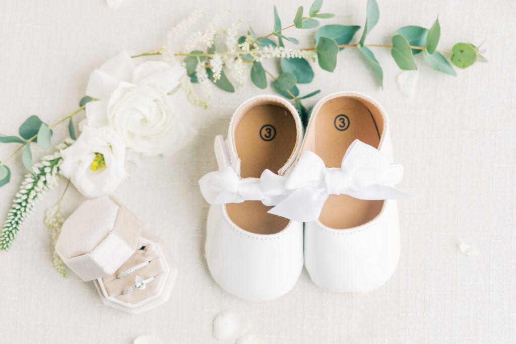 Tiny flower girl shoes posed with bride and grooms rings